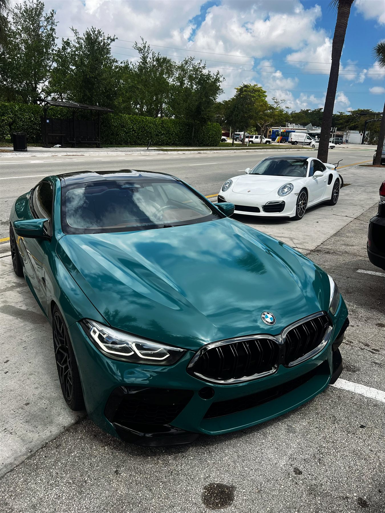 Green BMW performance car with white Porsche in the background